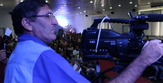 José Roberto Moura manuseando filmadora em auditório.