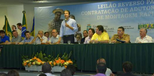 Camilo Santana em pé, falando ao microfone e atrás de uma mesa com nove pessoas distribuídas aos seus lados