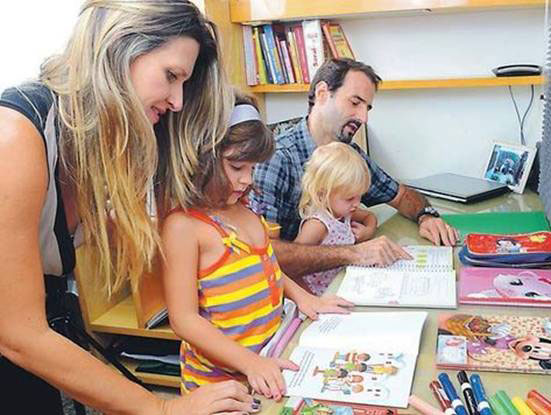 Um casal com duas crianças mostrando o conteúdo de livros abertos sobre uma mesa