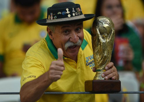 Clóvis Acosta vestindo amarelo e segurando uma réplica da taça da Copa do Mundo
