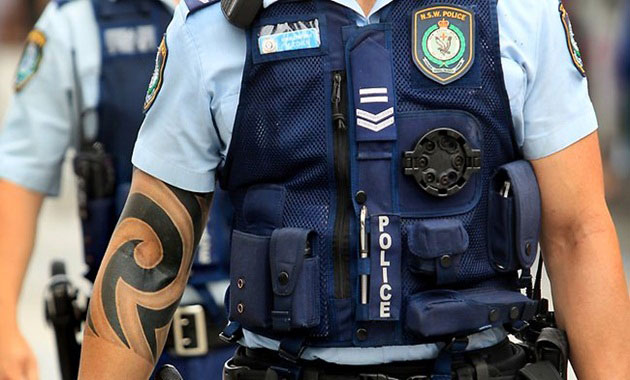 Foto do tronco de um policial fardado com uma tatuagem no braço direito