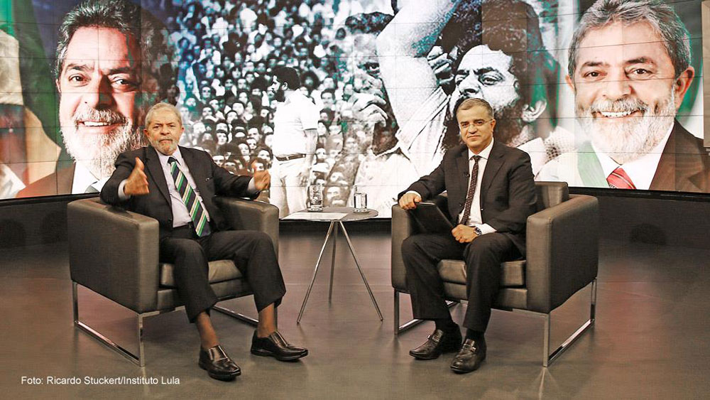 Lula e Kennedy Alencar sentados em estúdio e ao fundo imagens de Lula