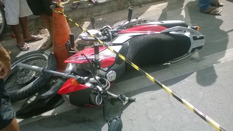 Motocicleta com guidão danificado e caída ao chão, próxima a acone com cordão de isolamento