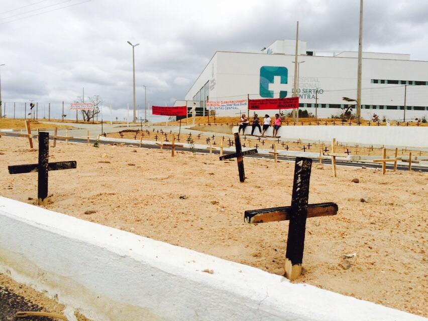 Várias cruzes de madeira fincadas ao chão na frente do Hospital Regional do Sertão Central
