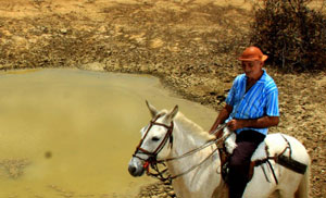 Homem a cavalo próximo a um açude com baixo nível de água.