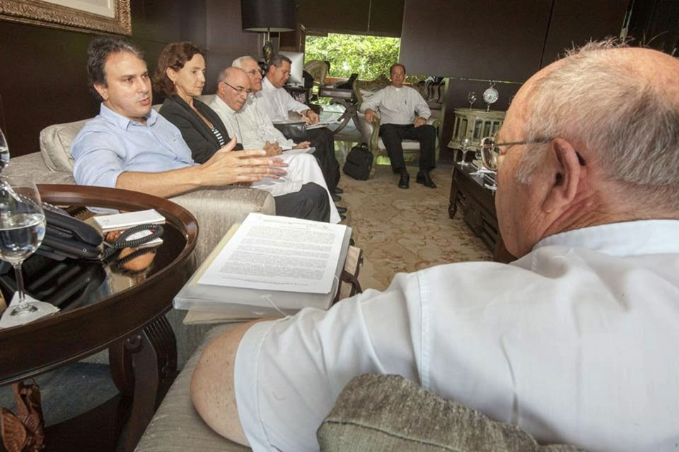 Governador Camilo Santana sentado ao sofá junto com representantes da CNBB