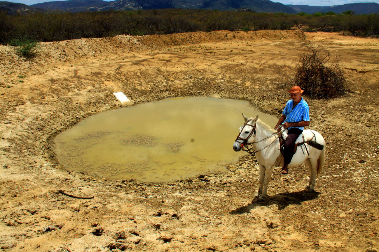 Homem a cavalo próximo a um açude com baixíssimo nível de água.