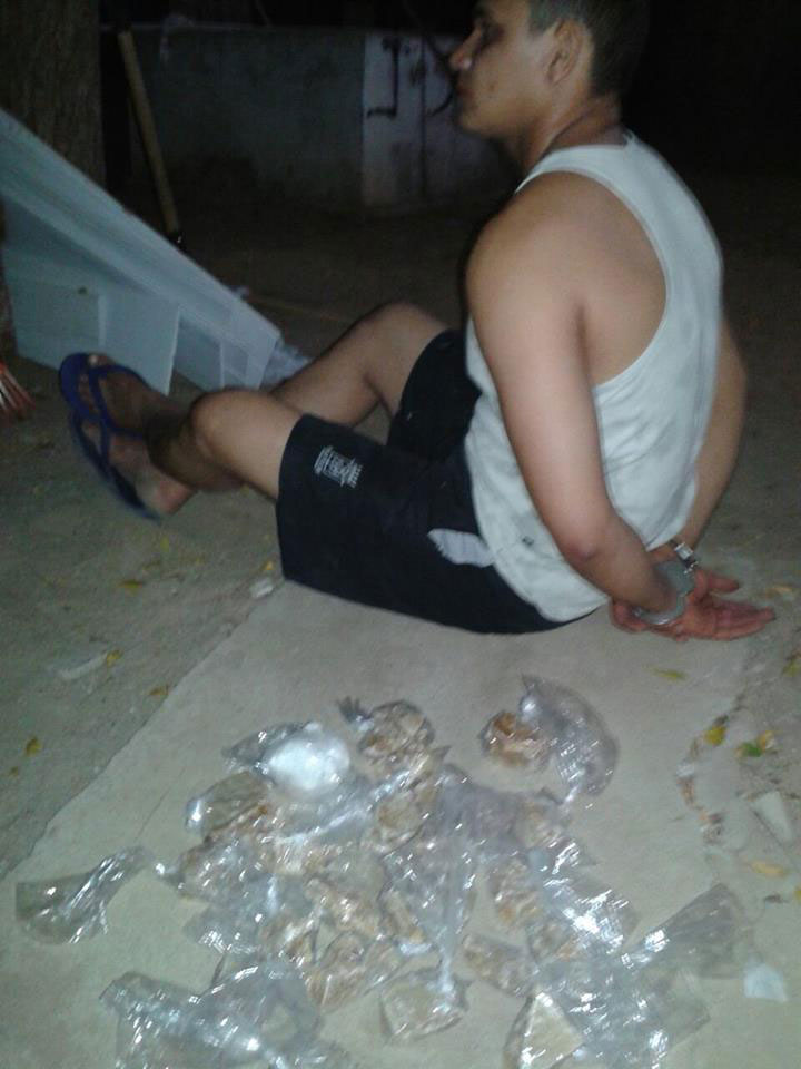 Francisco José de Assis Filho sentando no chão com as mãos algemadas atrás do corpo e pacote de drogas ao lado