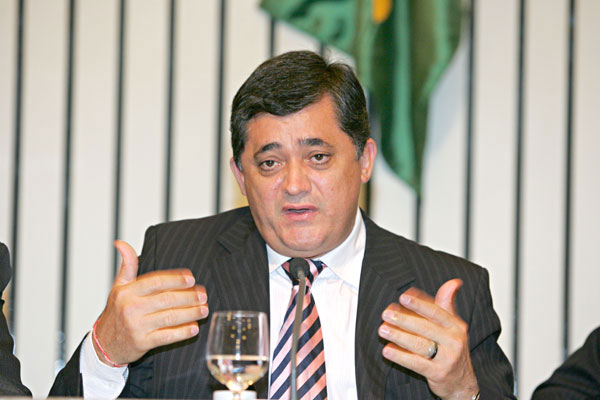 José Guimarães falando ao microfone gesticulando com as mãos abertas a altura do peito.