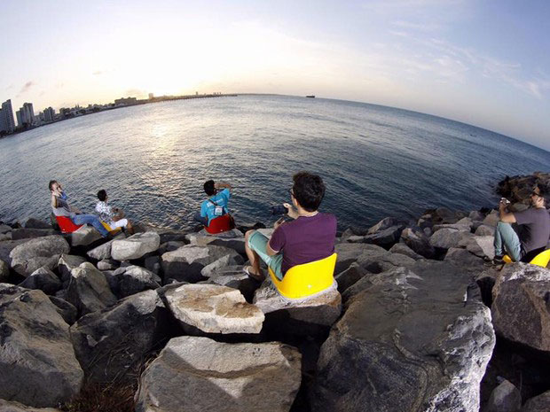 Pessoas sentadas em frente ao mar observando o pôr do sol.