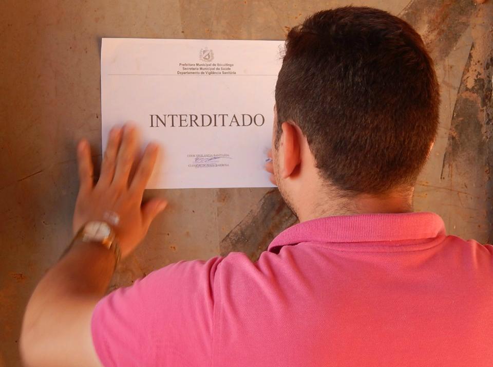 Homem fixando papel em parede com o letreiro: Interditado
