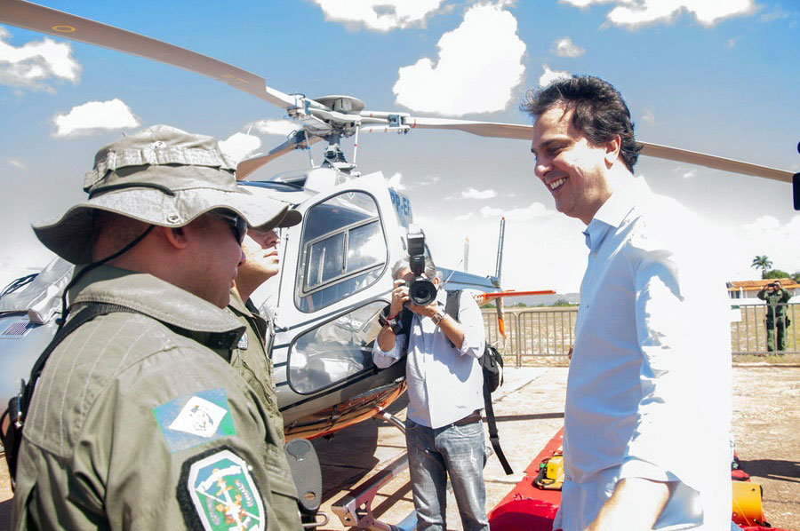 Governador Camilo Santana em frente a dois integrantes do Ciopaer. Ao fundo um helicóptero e um fotógrafo.