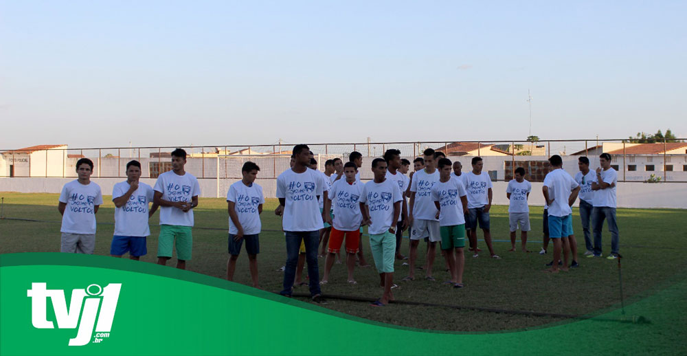 Jovens vestindo camisas brancas com mesma estampa andando aleatoriamente pelo campo.