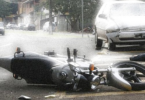 Moto caída no chão em primeiro plano e carro amaçado em segundo plano
