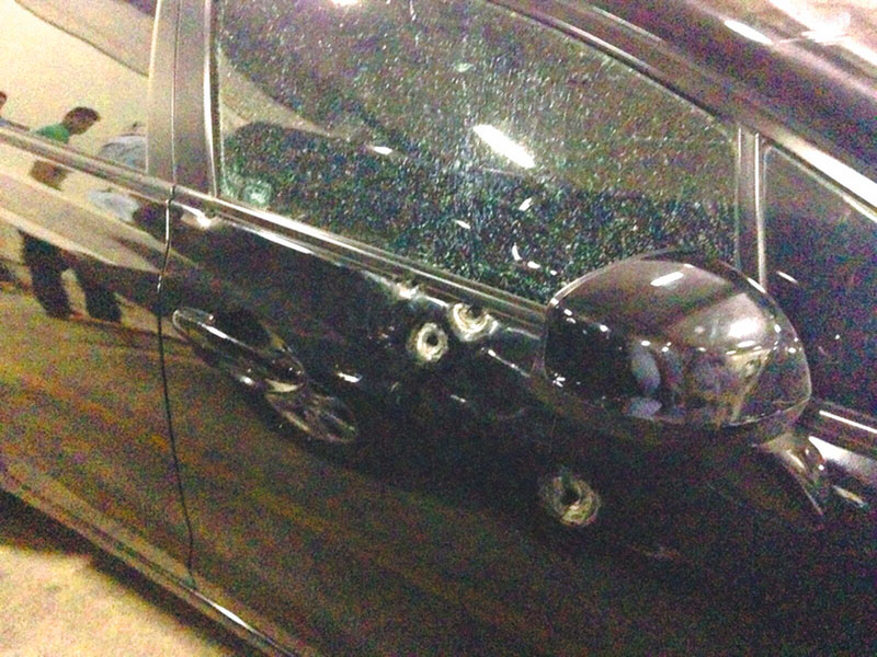 Visão parcial de carro preto com três marcas de bala na porta