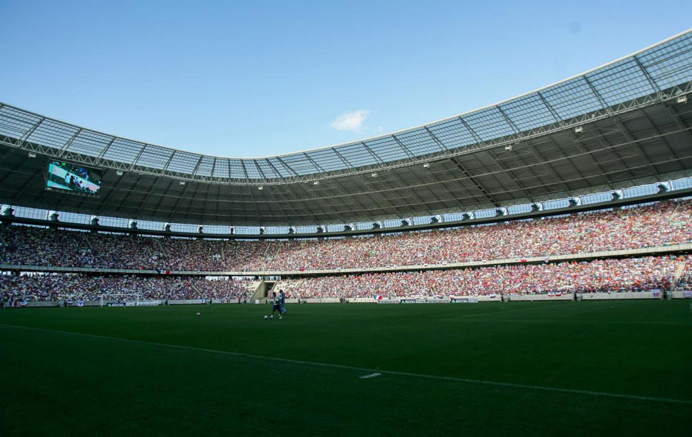 Foto registrada no grampo de um estádio de futebol com a arquibancada lotada e apenas dois jogadores no campo.