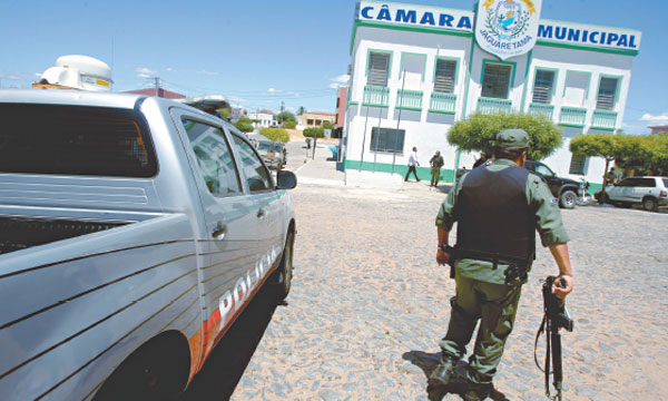 Viatura ao lado, policial armado andando em frente ao prédio da Câmara Municipal de Jaguaretama