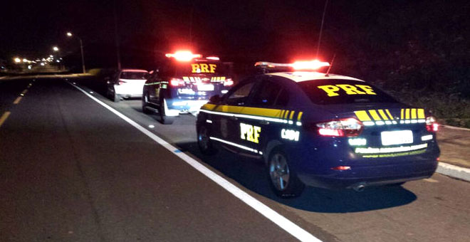 Dois carros da Polícia Rodoviária Federal e um de passeio, todos estacionados no acostamento de uma rodovia.