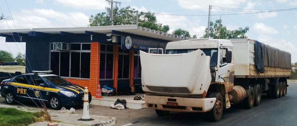 Caminhão estacionado, com o capô aberto, em frente a uma unidade da Policia Rodoviária Federal.