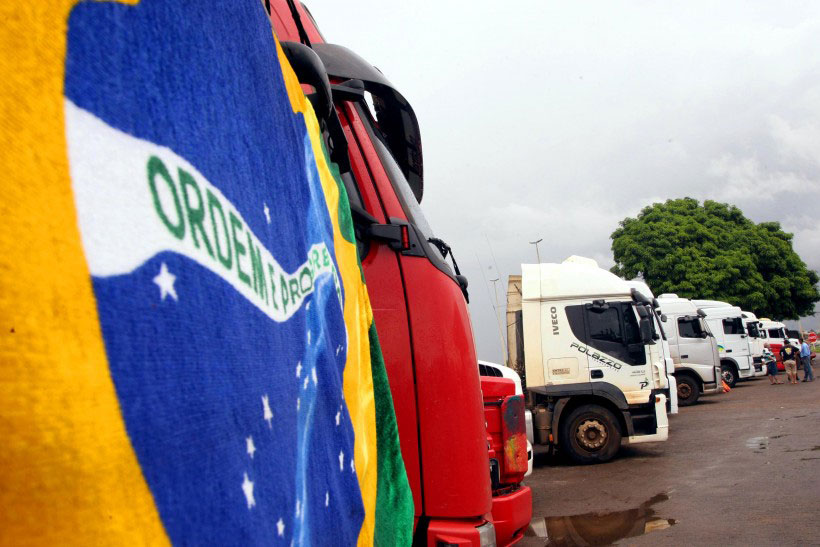 Bandeira do Brasil em primeiro plano e ao fundo caminhões alinhados lado-a-lado