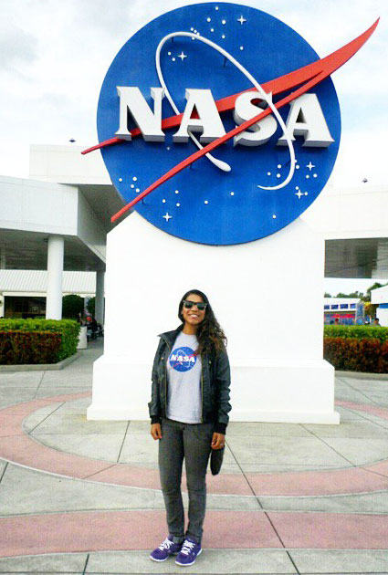 Marcela Alves posando para foto em frente a grande estrutura com logotipo da NASA