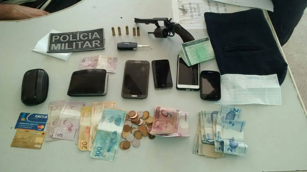 Dinheiro, revólver, celulares, cartões, carteira e documentos em cima de mesa