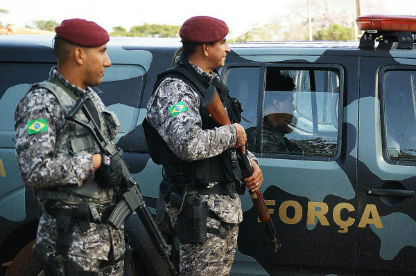 Dois soldados, armados, ao lado de veículo militar