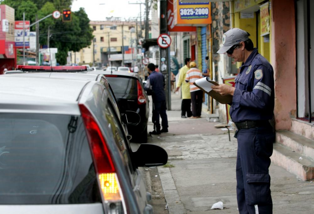 Agente de Trânsito escrevendo com apoio de uma prancheta em frente a um veículo estacionado