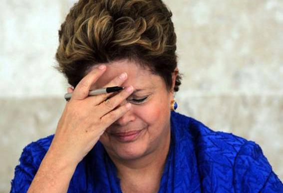 Dilma segurando caneta entre os dedos e com a mão no rosto, com expressão de desconforto