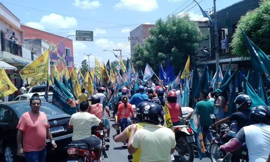 Muitas pessoas em uma rua com bandeiras, atrás pessoas em motocicletas.