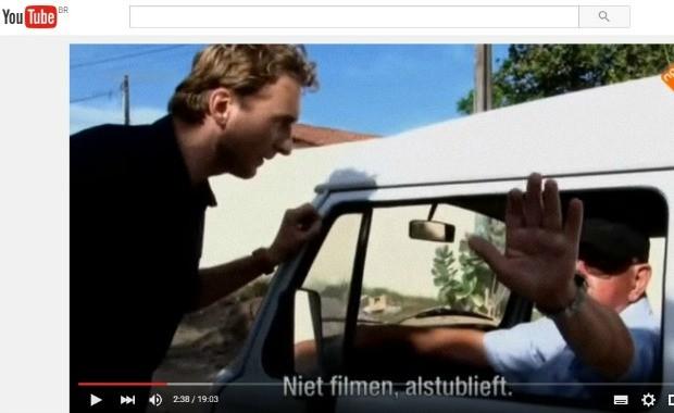 Imagem de vídeo com homem em pé ao lado de um carro e o motorista com a mão aberta tentando cobrir a câmera.