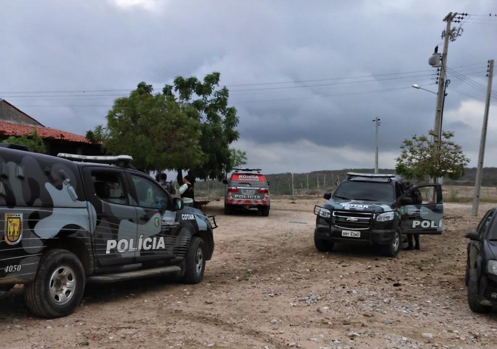 Três veículos da Polícia estacionados em estrada de terra na frente de uma casa.
