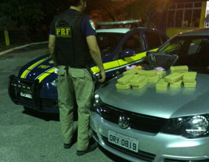 Carros da polícia federal e o utilizado pelo indivíduo perseguido, sendo o último com pacotes de pasta base de cocaína. Policial de costa entre os carros