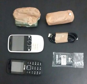 Dois pacotes de drogas, dois celulares e um carregador sob um fundo preto.