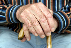 Mãos de um idoso sobre uma bengala de madeira