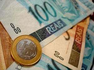 Uma moeda no valor de um real e três cédulas de dinheiro sendo duas no valor de 100 reais e uma no valor de 50