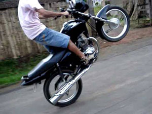 Homem sobre uma motocicleta com o pneu dianteiro erguido