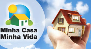 Logotipo do projeto Minha Casa Minha Vida e a foto de uma mão segurando uma casa. Ao fundo um céu com poucas nuvens.