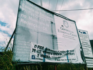 Placa com informações sobre obra abandonada e faixa de protesto presa a ela