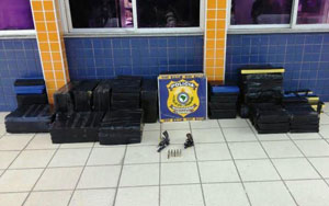 Placa com o brasão da Policia Rodoviária Federal, tabletes de maconha e dois revolveres.