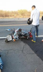 Motocicleta destruída em rodovia e homem com capacete no braço andando em volta do veículo
