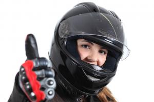 Mulher com capacete e roupa de motociclista sinalizando positivamente com o polegar